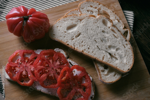A rustic flat lay featuring slices of homemade artisan bread, fresh heirloom tomato, peppers on a wooden kitchen table. Natural light and cozy farmhouse aesthetics