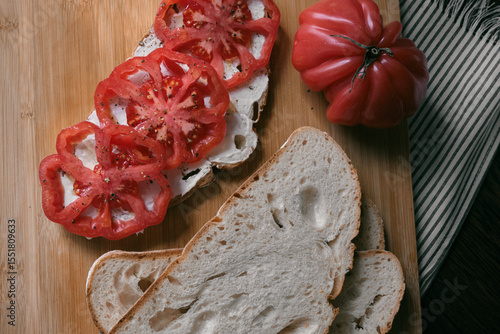 A rustic flat lay featuring slices of homemade artisan bread, fresh heirloom tomato, peppers on a wooden kitchen table. Natural light and cozy farmhouse aesthetics