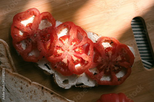 A rustic flat lay featuring slices of homemade artisan bread, fresh heirloom tomato, peppers on a wooden kitchen table. Natural light and cozy farmhouse aesthetics