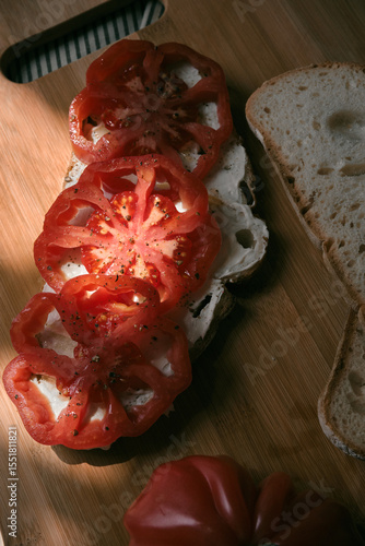 A rustic flat lay featuring slices of homemade artisan bread, fresh heirloom tomato, peppers on a wooden kitchen table. Natural light and cozy farmhouse aesthetics