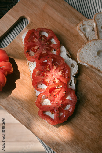 A rustic flat lay featuring slices of homemade artisan bread, fresh heirloom tomato, peppers on a wooden kitchen table. Natural light and cozy farmhouse aesthetics