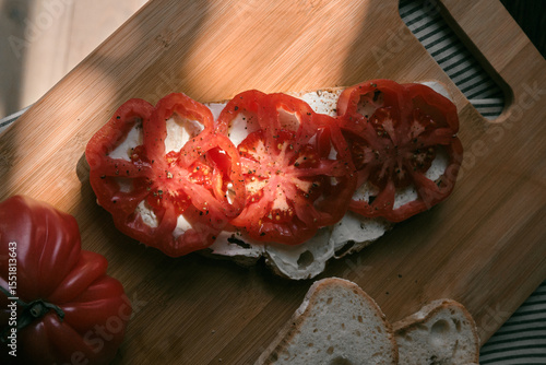 A rustic flat lay featuring slices of homemade artisan bread, fresh heirloom tomato, peppers on a wooden kitchen table. Natural light and cozy farmhouse aesthetics