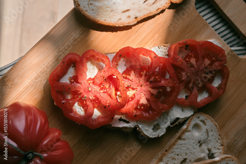 A rustic flat lay featuring slices of homemade artisan bread, fresh heirloom tomato, peppers on a wooden kitchen table. Natural light and cozy farmhouse aesthetics