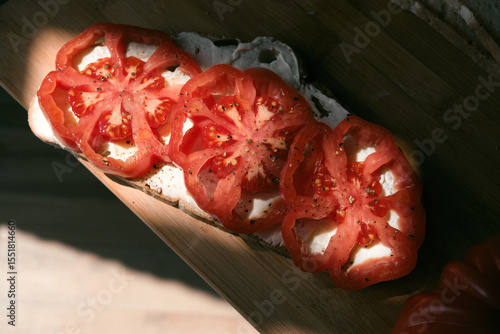 A rustic flat lay featuring slices of homemade artisan bread, fresh heirloom tomato, peppers on a wooden kitchen table. Natural light and cozy farmhouse aesthetics