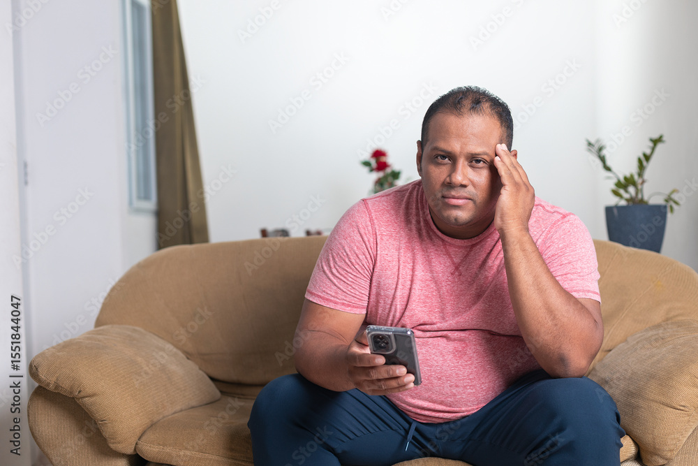 A man in a red shirt is sitting on a couch holding a remote control A man in a red shirt is sitting on a couch holding a remote control