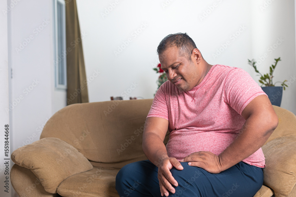 A man in a red shirt sits on a couch with his leg propped up A man in a red shirt sits on a couch with his leg propped up