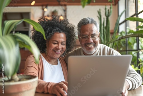 Portrait of a happy latino couple in their 70s ordering online looking in laptop
