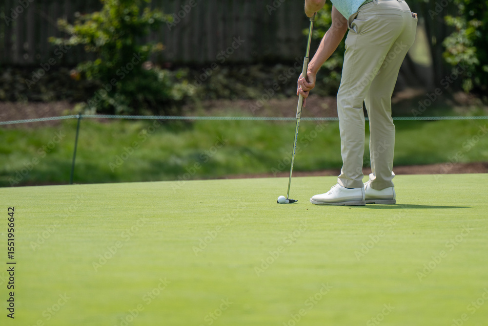 Obraz premium A golfer is captured mid-swing on a pristine green, preparing to putt a golf ball. The image focuses on the action, highlighting concentration in the sport.