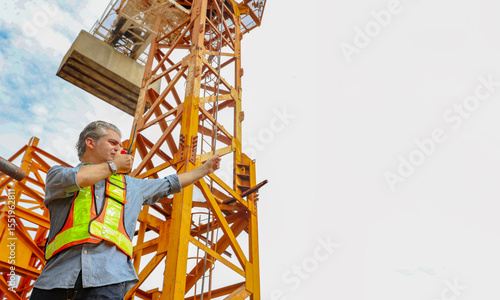 Fotografie Male workers control construction site : Workers control tower cranes, prepare to report for duty by radio communication, climb to high places with ladders with safety control systems