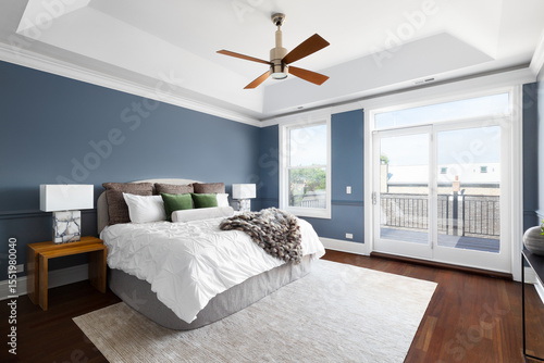 A bedroom with blue walls, white coffered ceiling with a modern fan, cozy bedding and decor, and dark hardwood flooring.
