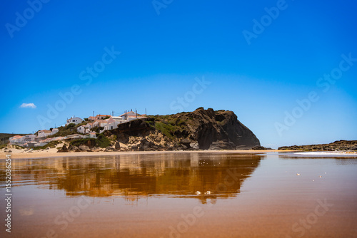Empty Monte Clerigo beach in Portugal. View of Monte Clerigo village and cliff reflected in water