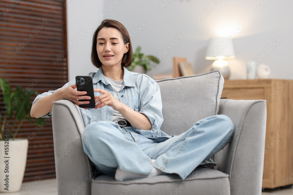 Obraz premium Woman using modern smartphone in armchair at home
