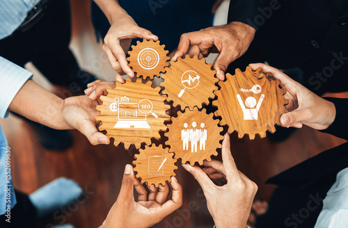 A diverse group of professionals collaborates over wooden gears featuring icons that symbolize business strategies, teamwork, and SEO, highlighting innovation and growth. Amity