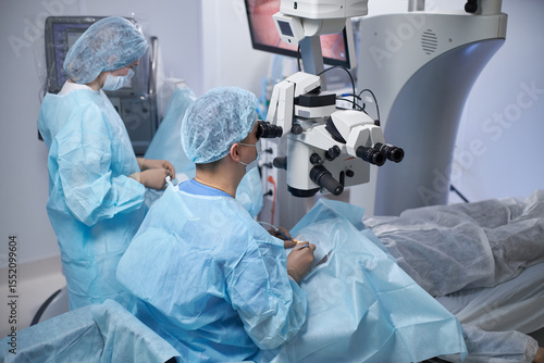 Obraz na plátně Middle aged man performing surgery using operating microscope while woman assist