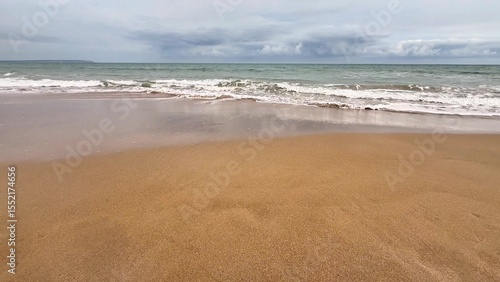 A tranquil beach scene depicting soft and warm sand, gentle waves lapping at the shore, and a cloudy horizon above
