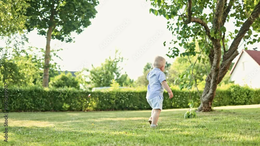 Toddler running on green grass. Active children's recreation. Smiling boy in shorts running and playing, having fun in the backyard on a sunny hot summer day. White boy playing hide and seek Toddler running on green grass. Active children's recreation. Smiling boy in shorts running and playing, having fun in the backyard on a sunny hot summer day. White boy playing hide and seek
