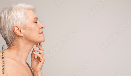 Aging gracefully. Closeup of beautiful senior lady touching skin on her neck. Side view panorama with empty space