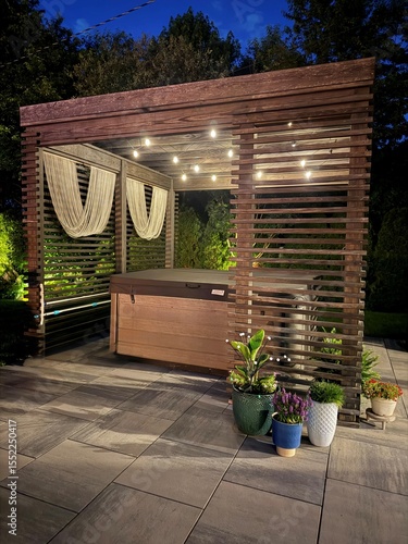 Gorgeous, luxury modern boho backyard design showcasing an outdoor pergola made from pine at sunset. Inside sits a hot tub spa with seats, lounger. Artsy decor and plant set the mood with LED lights.