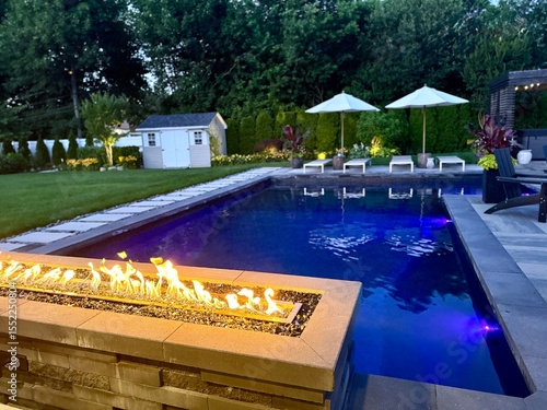 Gorgeous sunset backyard living space.  All Season - year round. Fire pit with cascading waterfall.  J shaped pool and sundeck.  Colored LED lights illuminate the pool - stunning display of design.