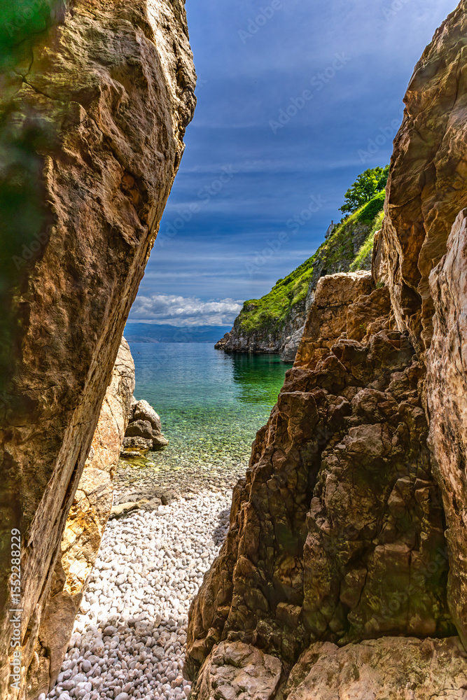 Fototapeta premium The crystal clear blue water of the Adriatic Sea, a hidden entrance to a small beach that is a tourist attraction KRK