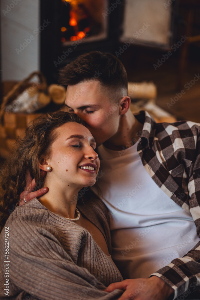 Happy young couple spending lazy weekend at home, embracing, kissing, enjoying near fireplace in the countryside cottage house, feeling relaxed and calm. Cozy home atmosphere, simple domestic life Happy young couple spending lazy weekend at home, embracing, kissing, enjoying near fireplace in the countryside cottage house, feeling relaxed and calm. Cozy home atmosphere, simple domestic life