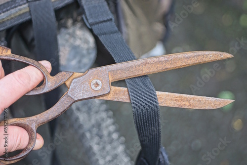 Behang hand holding old brown big rusty iron scissors cutting black strap on bag on sum