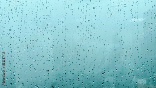 Raindrops on a glass window with a soft blue background, creating a moody and atmospheric texture.