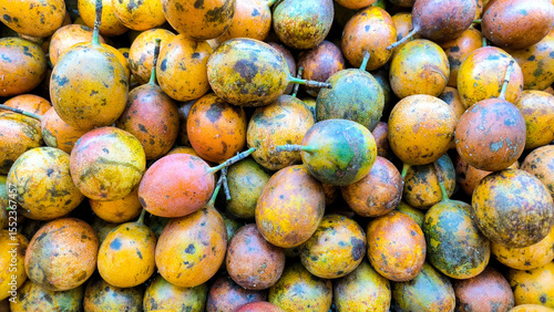 A pile of ripe passion fruits with colorful yellow, orange, and purple skins, freshly harvested and displayed in bulk.