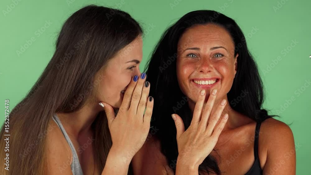 Cheerful female friends sharing secrets on vibrant green chromakey background Cheerful female friends sharing secrets on vibrant green chromakey background