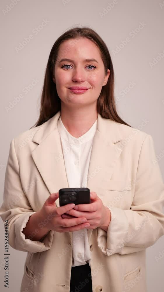 Confident young woman in a professional outfit engages with her smartphone in a bright, minimalist setting Confident young woman in a professional outfit engages with her smartphone in a bright, minimalist setting