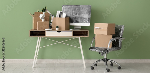 Workplace with cardboard boxes and chair near green wall in office on moving day