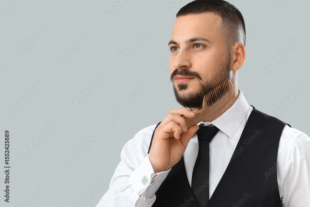 Handsome young bearded man combing beard on grey background Handsome young bearded man combing beard on grey background