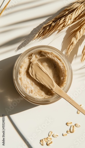 Oat mask cream on jar with wooden spoons, beige vertical background