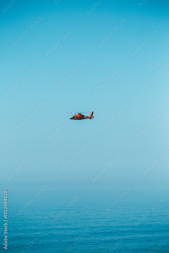 Bright Orange Helicopter Flying Over Calm Blue Ocean Bright Orange Helicopter Flying Over Calm Blue Ocean