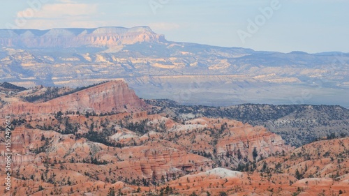 Expansive view of Bryce Canyon’s colorful ridges and pine-dotted cliffs, with layered mesas and mountains in soft evening light.