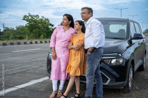 Indian couple showing nature or birds to little girl kid in front of car - concept of family traveling, vacation and weekend summer holidays