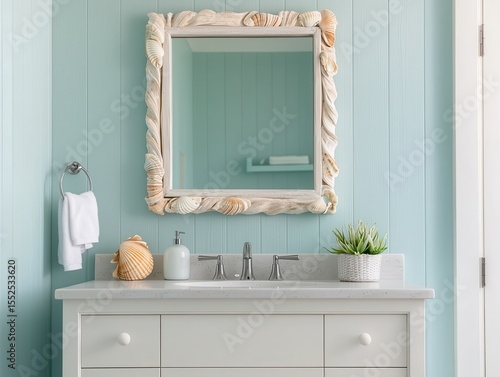 A coastal-themed bathroom vanity with a seashell-framed mirror, light blue walls, white cabinet, and minimal decor featuring a plant and soap dispenser.