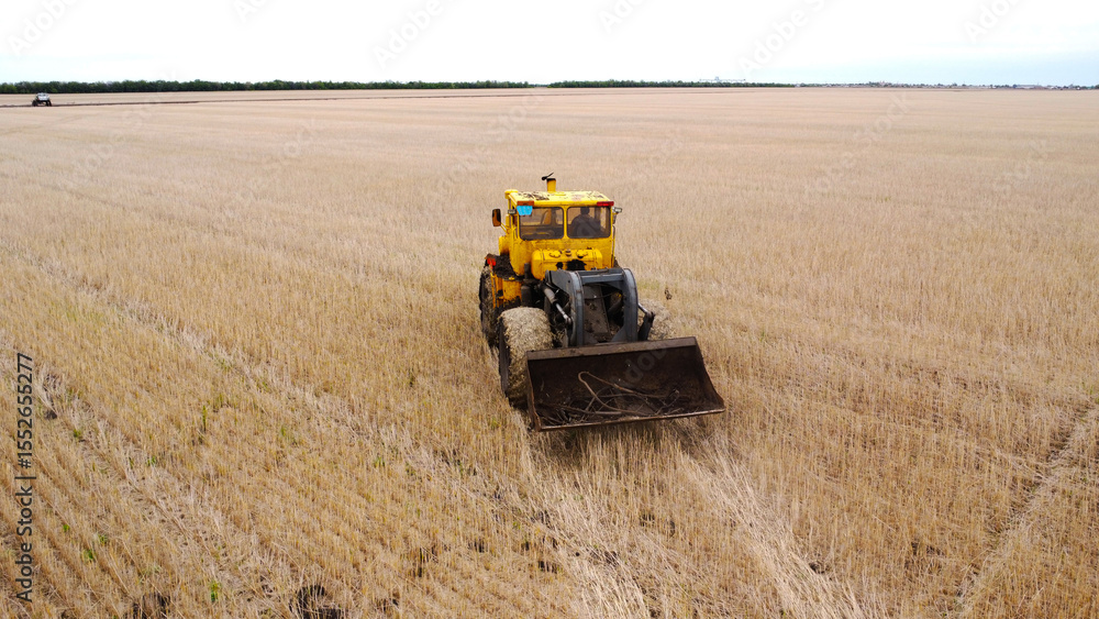 Obraz premium Areal view of yellow tractor on harvested farm field