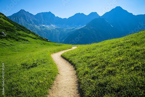 Winding dirt path through lush green alpine meadows towards majestic blue mountains