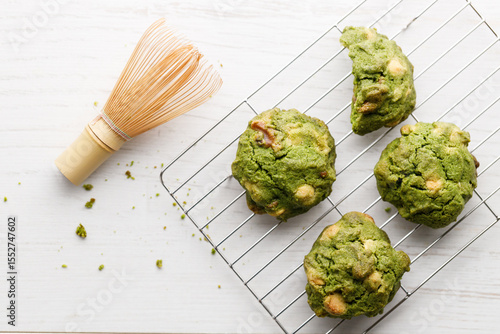 Closeup of fresh baked matcha cookies with Chasen, bamboo whisk, on white wooden background.