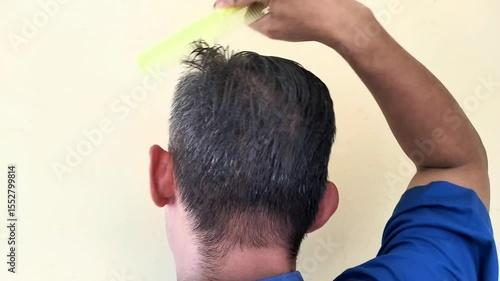 back of head, An Asian man is combing his hair with a light green comb.
