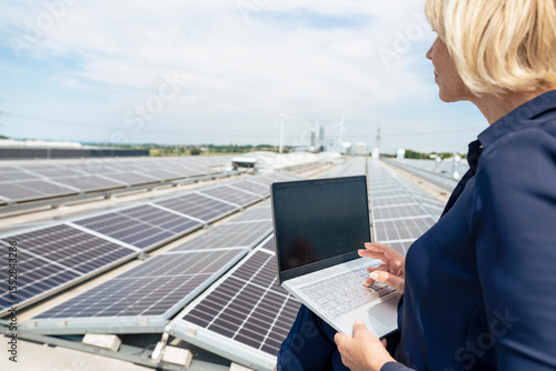 Senior businesswoman using laptop in front of solar panels on rooftop