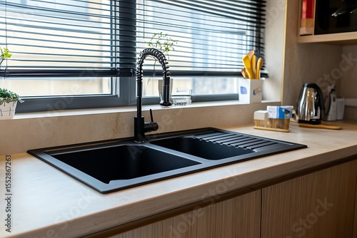Modern kitchen interior with dark sink, faucet, window, and light wood cabinets