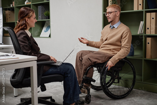 Quadro em tela Caucasian young adult man with disability sitting in wheelchair talking to femal