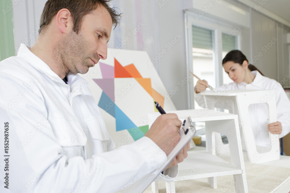 Fototapeta premium foreman writing on clipboard while female apprentice paints