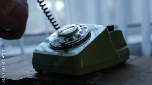 Close-up view of a hand picking up the telephone receiver and dialing numbers on an old rotary phone. Retro plastic phone.