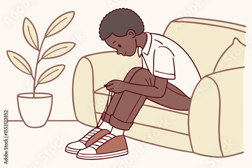Front view of African american boy tying shoelaces on sofa