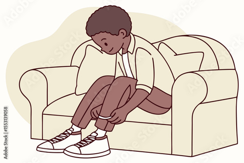 African American boy tying his shoelaces while sitting on a sofa, front view