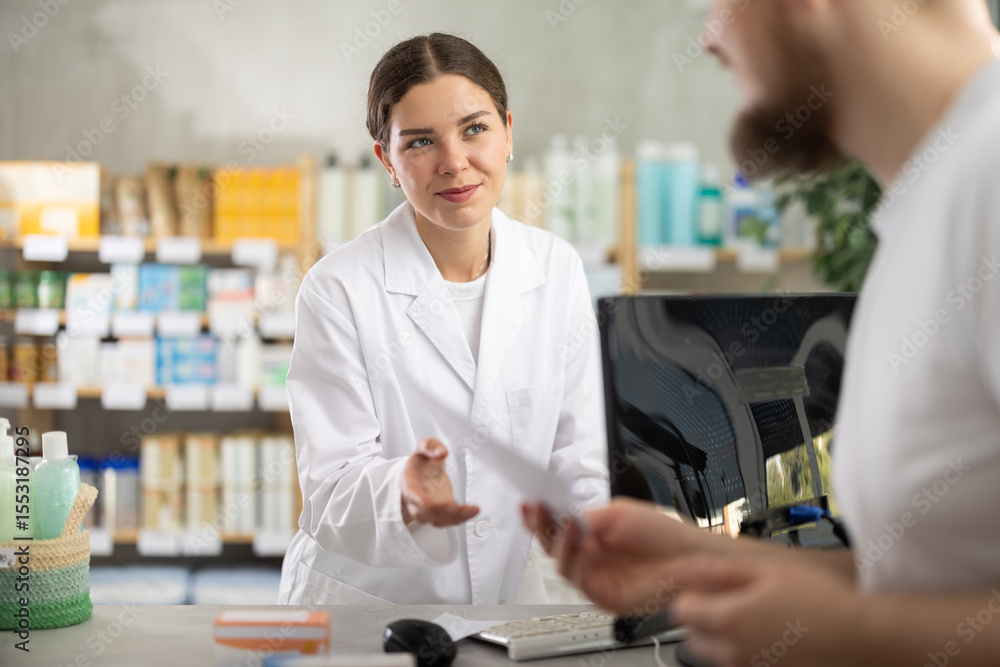 Obraz premium Male customer holding prescription searches for medicine in pharmacy. Female pharmacist offers to help find information on a computer