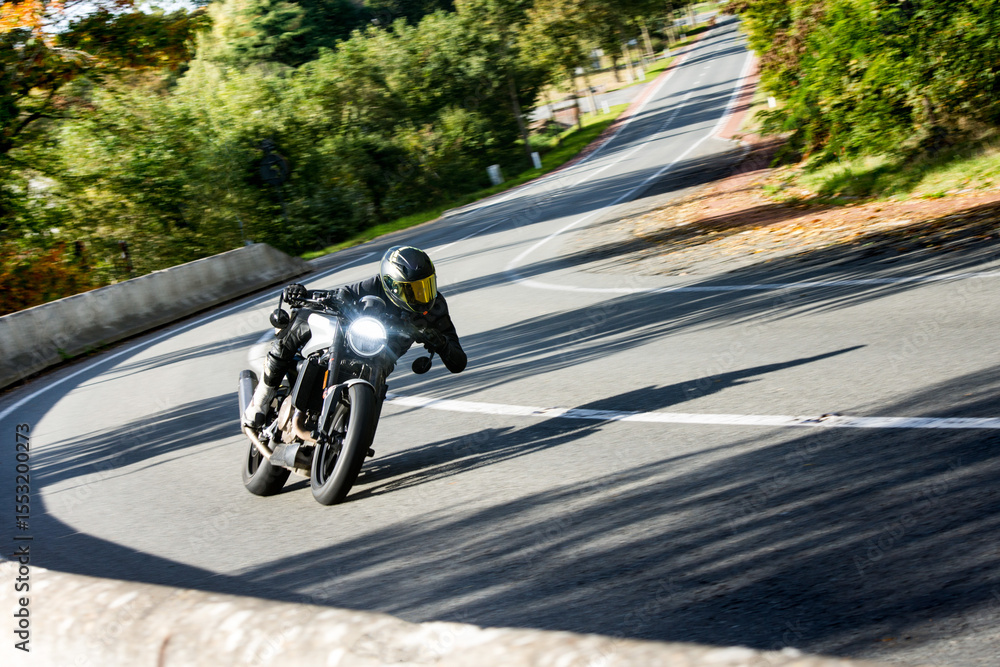 Obraz premium A skilled motorcyclist leans into a sharp turn on a scenic, tree-lined road, showcasing speed and control.